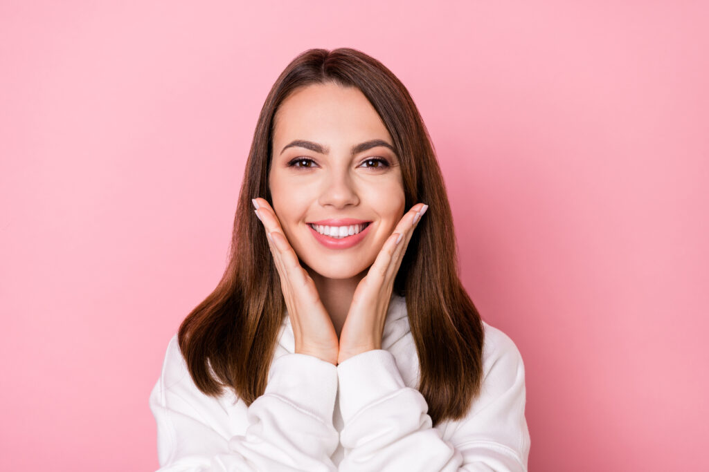 Photo of attractive happy young pretty woman hold hands face cheeks teeth isolated on pink color background