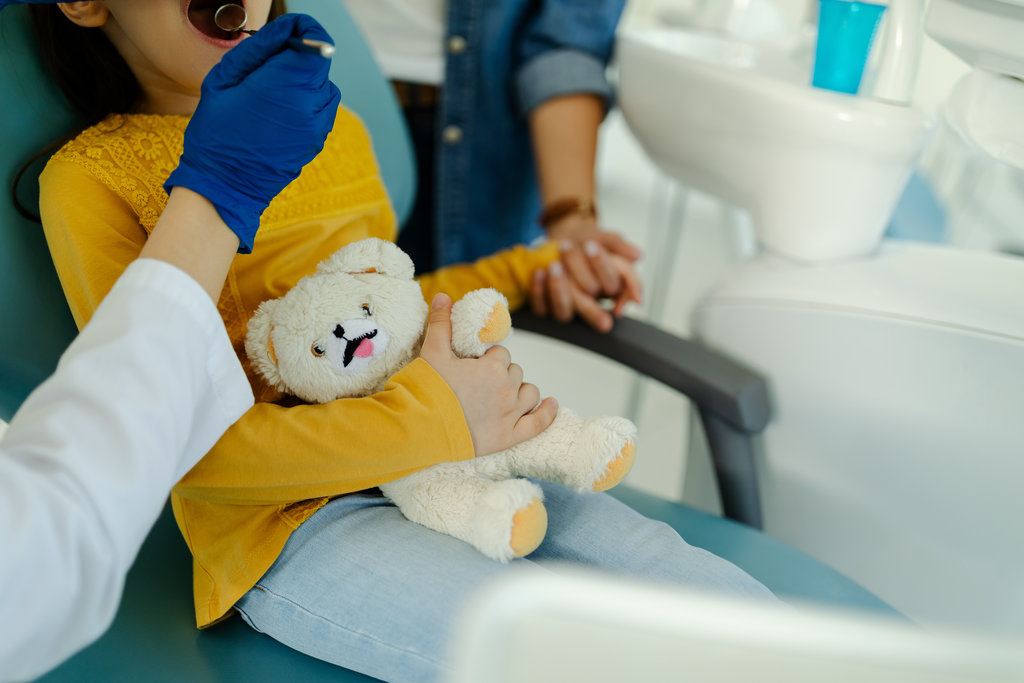 Close up photo of a mother holding the hand of her daughter who is visiting the dentist and thus supporting her.