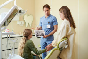 Male Dentist Showing Dental X-Ray to Teenager Girl with Mother