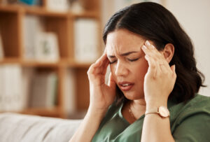 Stress, headache and woman on a sofa with vertigo, brain fog or burnout in her home. Migraine, anxiety and female in a living room with problem fail or crisis, fatigue or mental health problem.