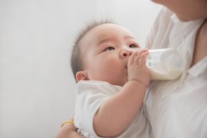 mother holding and feeding baby from milk bottle.portrait of cute baby being fed by her mother using bottle. loving woman giving drink milk to her son. mother feeding newborn baby from bottle at home