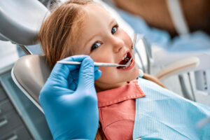 Children's dentistry. Close-up portrait of a girl sitting in a dental chair and having her teeth treated. A doctor in gloves holds instruments.