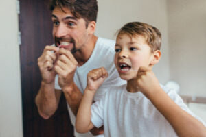 Father and child cleaning teeth with dental floss together