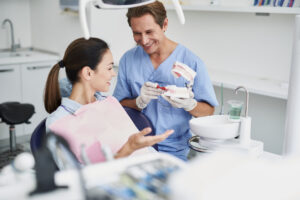 Smiling dentist showing teeth model to young woman